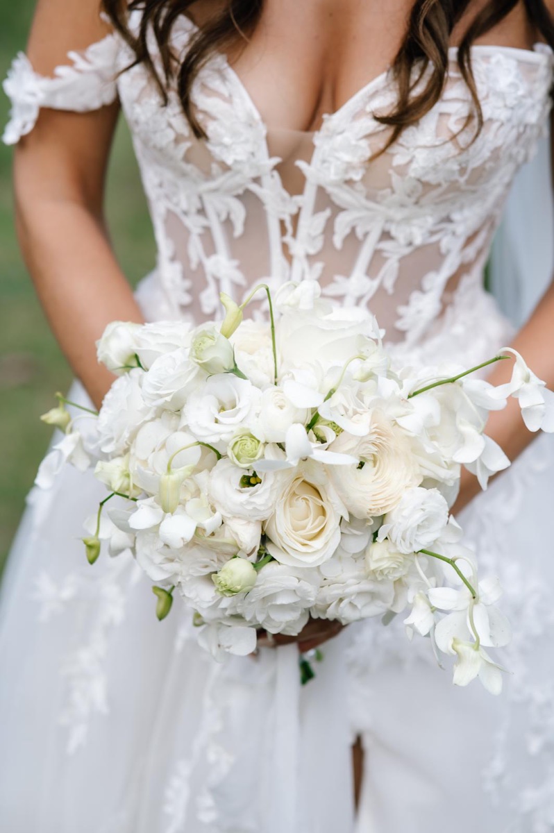Braut mit elegantem, ganz in Weiß gehaltenem Brautstrauß aus Rosen und Orchideen